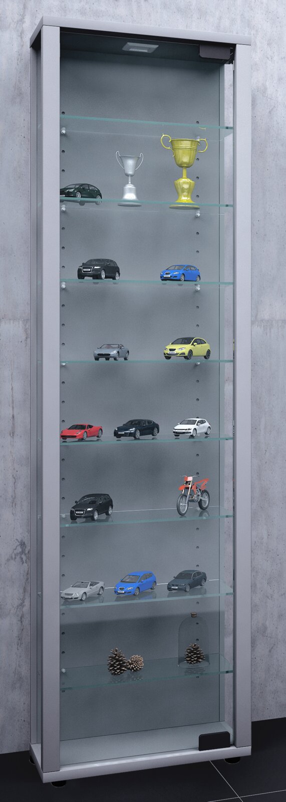 Hohe Glasvitrine mit Aluminiumrahmen und Glaseinlegeböden, bestückt mit Modellautos, Pokalen und Dekoration; frontale Ansicht leicht von links.