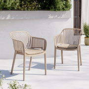 Zwei beigefarbene Outdoor-Stühle aus Kunststoff mit schlitzförmiger Rückenlehne und Sitzkissen auf heller Terrasse vor weißer Wand und Grünpflanzen, Perspektive: frontale leicht seitliche Ansicht auf Augenhöhe