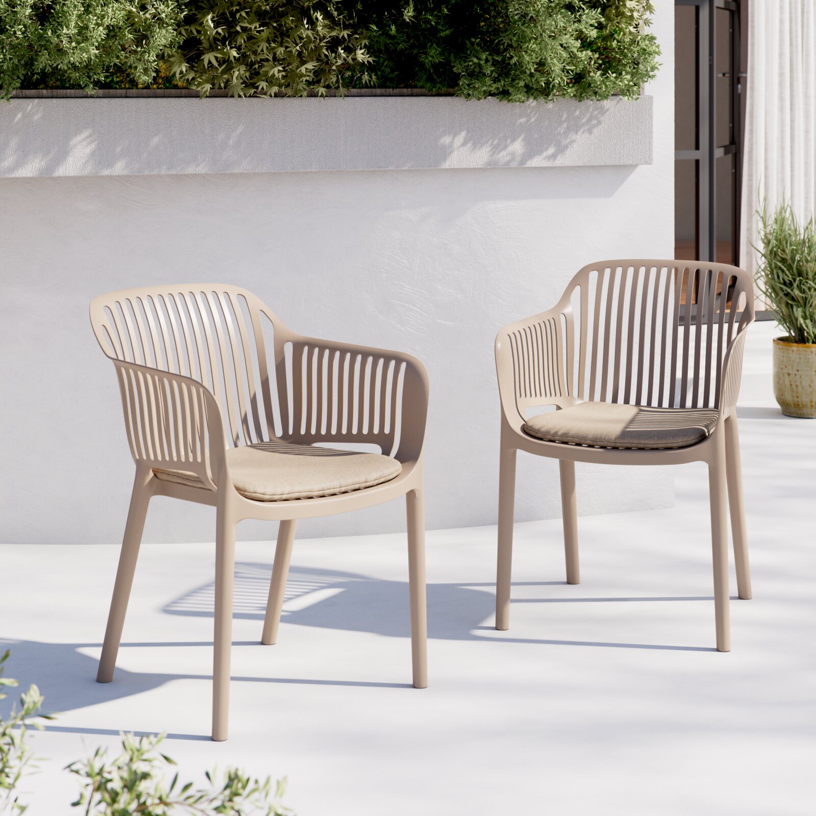 Zwei beigefarbene Outdoor-Stühle aus Kunststoff mit schlitzförmiger Rückenlehne und Sitzkissen auf heller Terrasse vor weißer Wand und Grünpflanzen, Perspektive: frontale leicht seitliche Ansicht auf Augenhöhe
