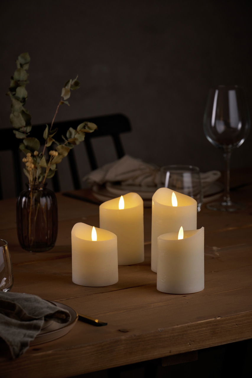 Vier LED-Kerzen in warmem Licht auf einem gedeckten Tisch, seitliche Perspektive.