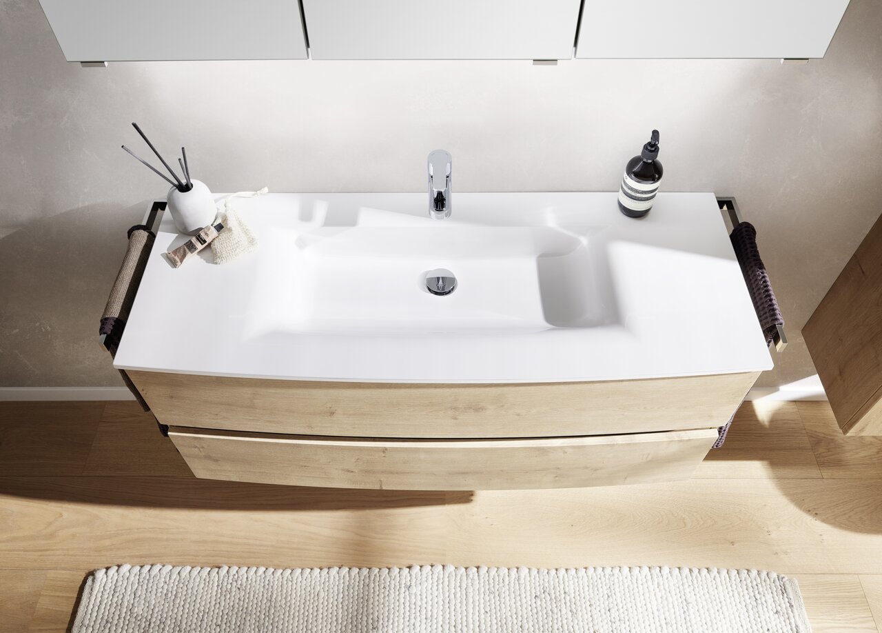 Moderne badkamercombinatie met houtlook en een witte wastafel, gezien van bovenaf.