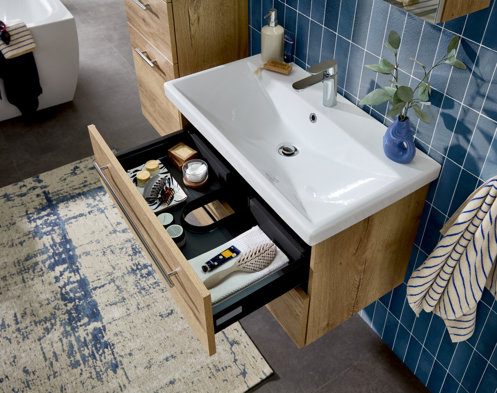 Badezimmer-Waschtisch mit weißem Keramikbecken und Holz-Unterschrank, Schublade geöffnet mit Organizer-Einsatz, Draufsicht schräg von oben.