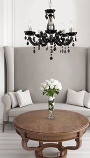 Eleganter schwarzer Kronleuchter mit sechs Armen und dekorativen Kristallen, hängend über einem runden Holztisch in einem stilvollen Wohnzimmer. Perspektive von unten.