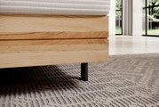 Nahaufnahme eines Boxspringbettes mit Holzrahmen und schwarzem Bein, seitliche Perspektive.