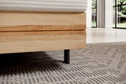 Nahaufnahme eines Boxspringbettes mit Holzrahmen und schwarzem Bein, seitliche Perspektive.