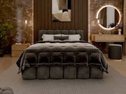 Een luxe gestoffeerd bedframe in een stijlvol ingerichte slaapkamer, gezien vanaf de voorkant. Het bed is voorzien van een donkere, doorgestikte deken en verschillende kussens. Op de achtergrond zijn een moderne wandbekleding, een ronde verlichte spiegel 