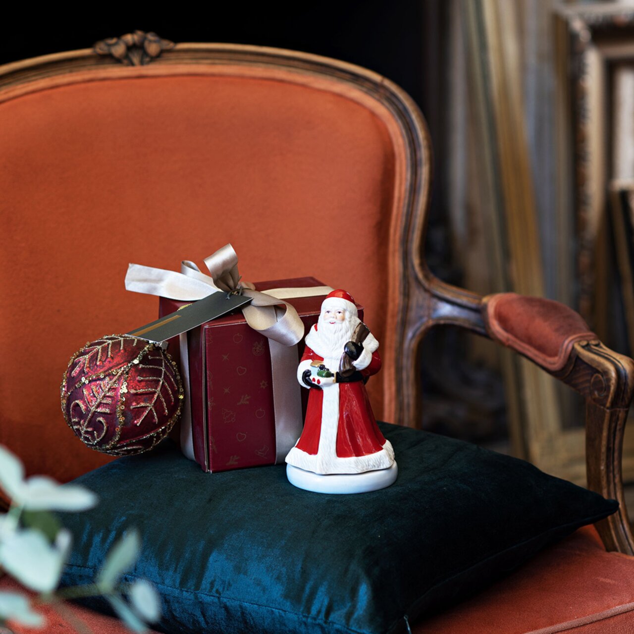 Muziekdoos met een ronddraaiende kerstman, geplaatst op een groen kussen voor een rode fauteuil, zijaanzicht