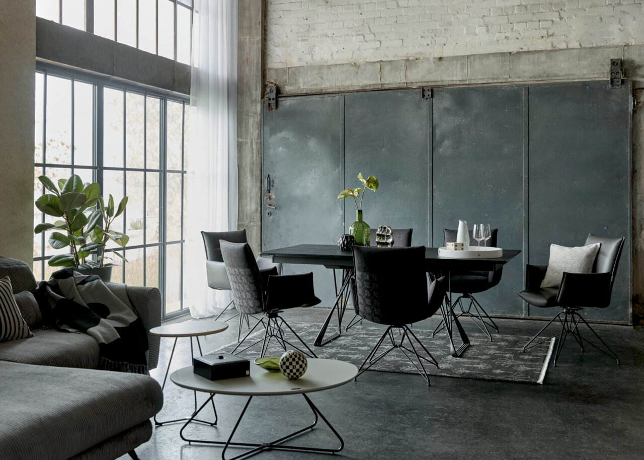 JOOP! Esstisch STUDIO J64 Industrial-Loft-Essbereich mit schwarzem Esstisch und sechs schwarzen Stühlen auf gemustertem Teppich, große Fenster links; Perspektive: leicht seitliche Weitwinkelansicht auf Tischgruppe