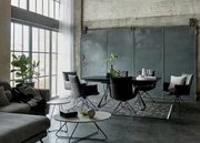 Industrial-Loft-Essbereich mit schwarzem Esstisch und sechs schwarzen Stühlen auf gemustertem Teppich, große Fenster links; Perspektive: leicht seitliche Weitwinkelansicht auf Tischgruppe