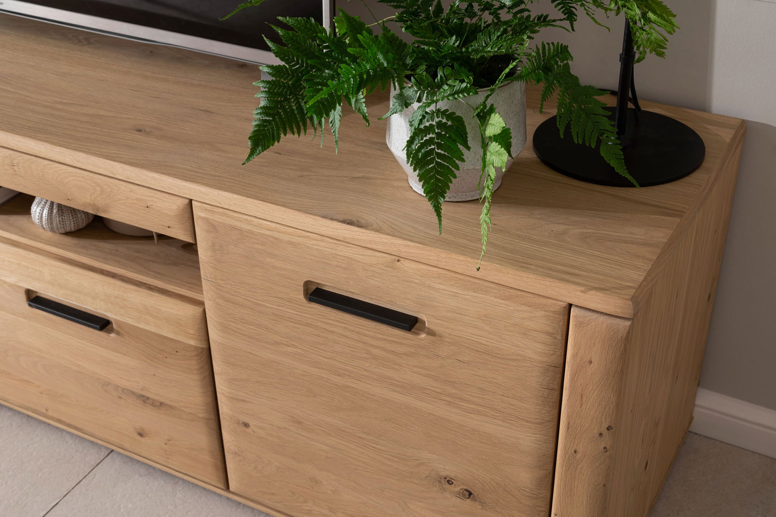 TV-Element aus Holz mit zwei Schubladen und einer Tür, dekoriert mit einer Pflanze, aus der Perspektive von oben rechts fotografiert.