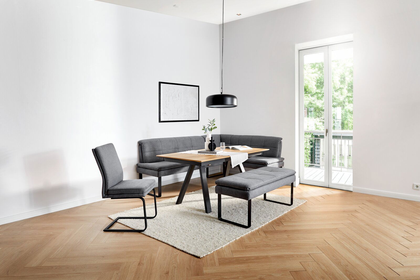 Moderner Esstisch mit grauen Polsterbänken und Stühlen in einem hellen Raum mit Blick auf eine Terrasse.