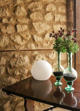 Kugelleuchte BULY 20 auf einem Holztisch vor einer Steinwand, seitliche Perspektive