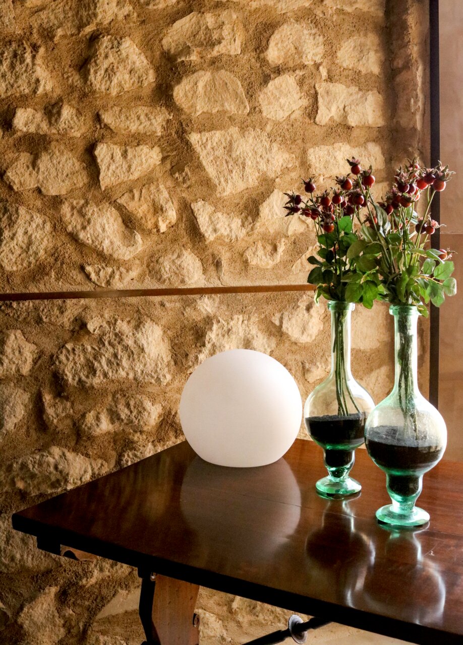 Kugelleuchte BULY 20 auf einem Holztisch vor einer Steinwand, seitliche Perspektive