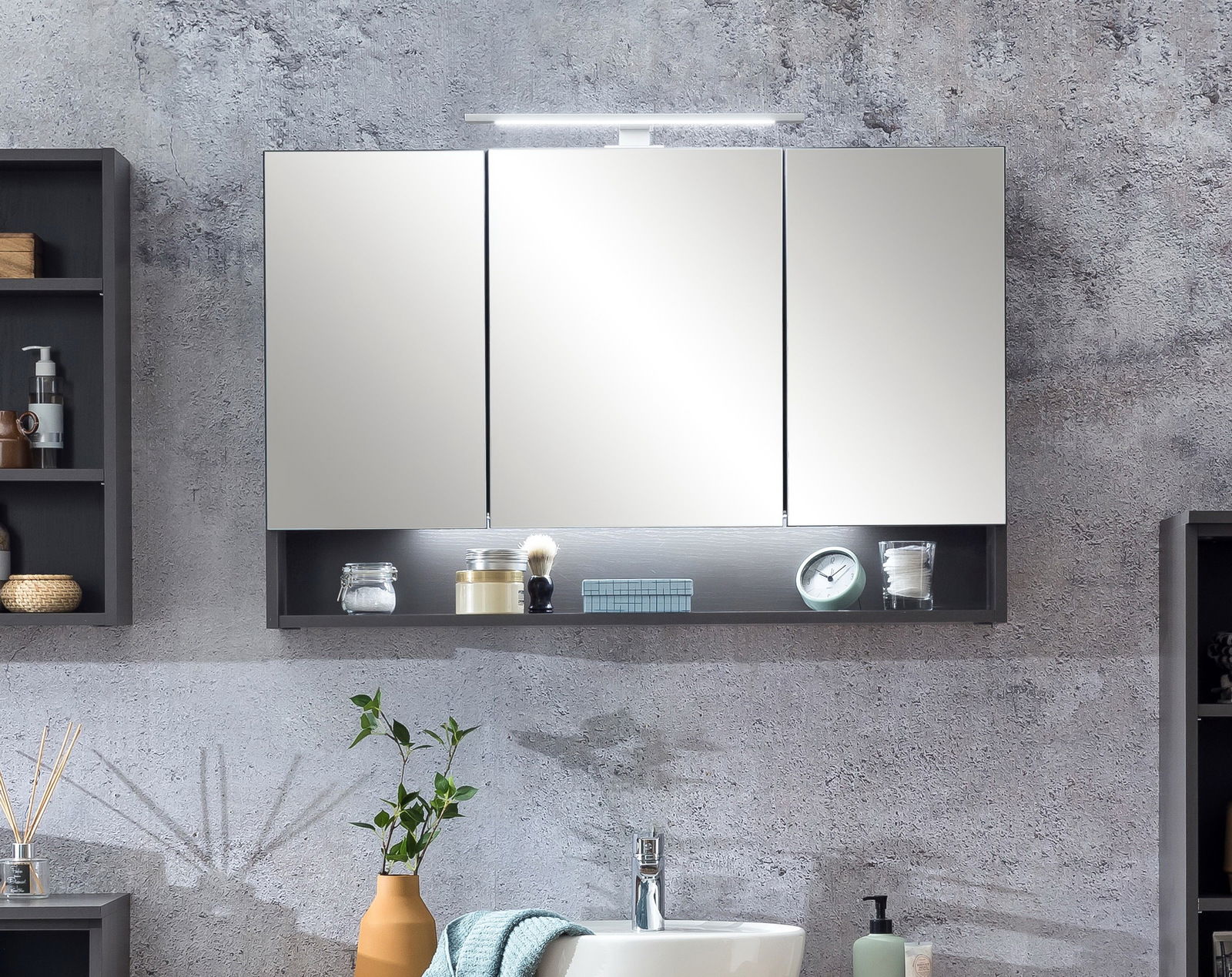 Moderner Spiegelschrank mit drei Türen und integrierter Beleuchtung, frontal betrachtet, mit offenen Regalfächern darunter.