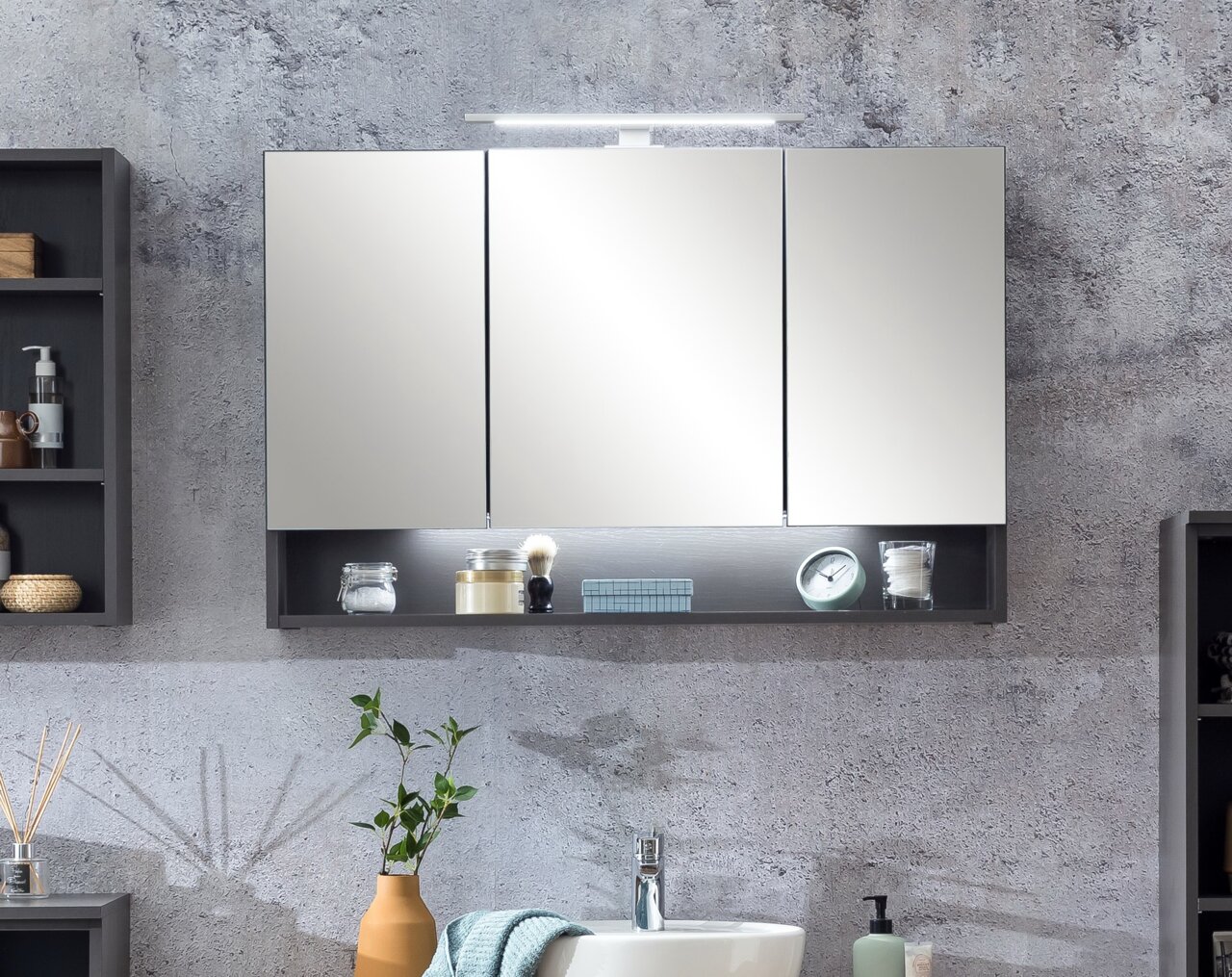 Moderner Spiegelschrank mit drei Türen und integrierter Beleuchtung, frontal betrachtet, mit offenen Regalfächern darunter.