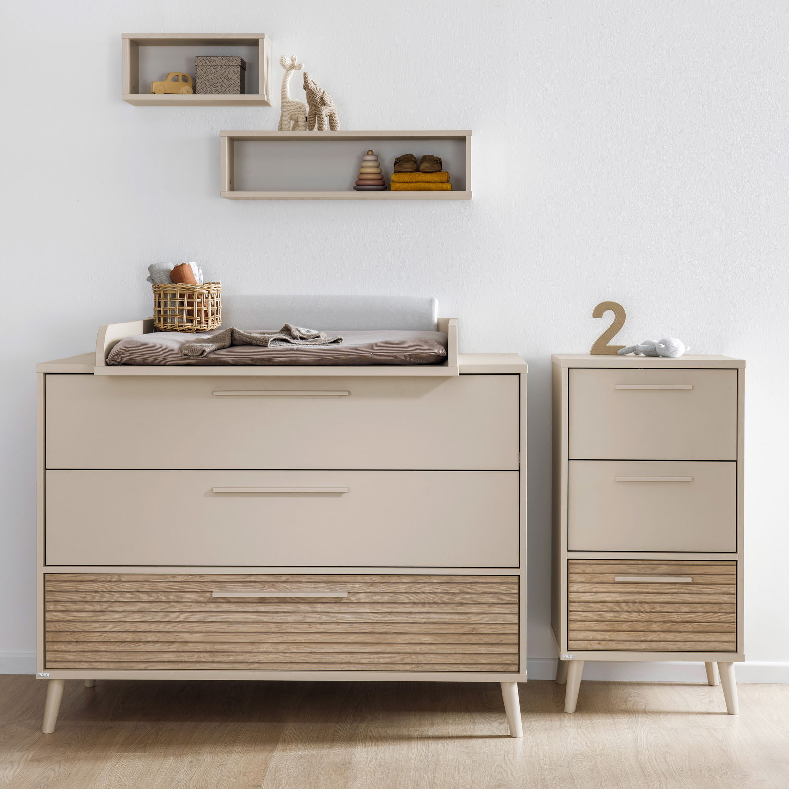 Breite Kommode mit Wickelaufsatz in modernem Design, frontal fotografiert, mit zusätzlichem schmalen Schrank und dekorativen Regalen an der Wand.