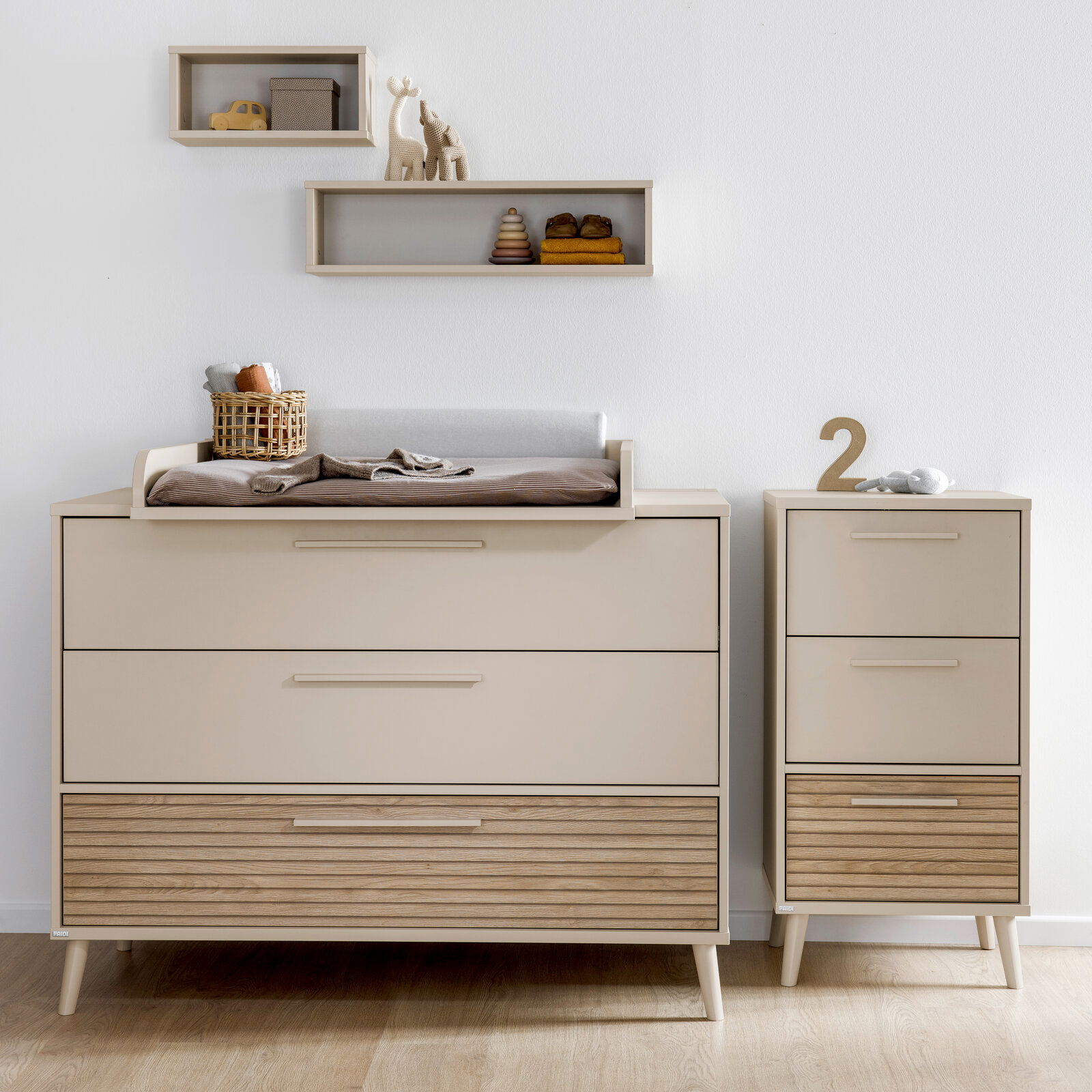 Breite Kommode mit Wickelaufsatz in modernem Design, frontal fotografiert, mit zusätzlichem schmalen Schrank und dekorativen Regalen an der Wand.