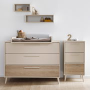 Breite Kommode mit Wickelaufsatz in modernem Design, frontal fotografiert, mit zusätzlichem schmalen Schrank und dekorativen Regalen an der Wand.