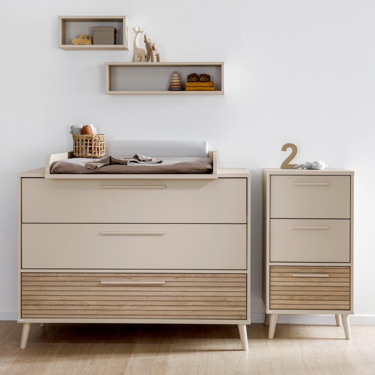 Breite Kommode mit Wickelaufsatz in modernem Design, frontal fotografiert, mit zusätzlichem schmalen Schrank und dekorativen Regalen an der Wand.