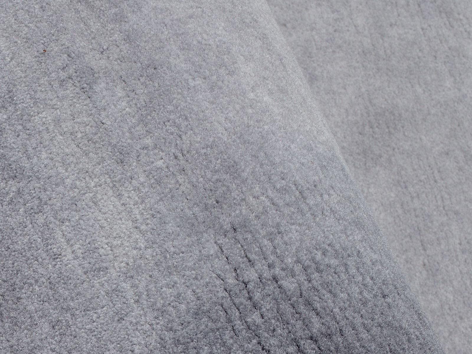 Nahaufnahme eines grauen Wollteppichs mit weicher Textur, schräg von oben fotografiert.
