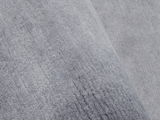 Nahaufnahme eines grauen Wollteppichs mit weicher Textur, schräg von oben fotografiert.