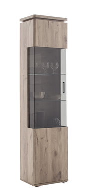 Hohe Vitrine aus hellem Holz mit Glasfront und schwarzem Griff, mit Glasböden und dekorierten Gläsern im Inneren, freigestellt auf weißem Hintergrund, Perspektive: frontale Ansicht leicht von links
