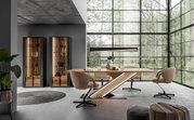 Een moderne eetkamer met een grote houten tafel en ledverlichting, omringd door draaistoelen en hoge vitrinekasten, met uitzicht op een groene buitenomgeving door grote ramen.