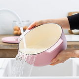 Rosa Gusseisen Bräter, rund, 26 cm, wird in einem Waschbecken unter fließendem Wasser gereinigt, seitliche Perspektive.