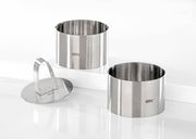 Zwei Edelstahlringe und ein Edelstahlpresser, frontal und leicht von oben betrachtet, ideal für Desserts oder Vorspeisen.