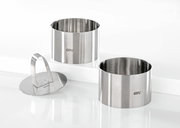 Zwei Edelstahlringe und ein Edelstahlpresser, frontal und leicht von oben betrachtet, ideal für Desserts oder Vorspeisen.