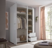 Offener weißer Kleiderschrank mit glänzenden Fronten, Kleiderstange, Regalböden und zwei Auszügen, seitliche Frontansicht im hellen Schlafzimmer neben großem Fenster mit rosa Vorhang
