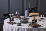 Elegante Tischszene mit einer grauen Salzmühle im Vordergrund, umgeben von stilvollem Geschirr und einer gedeckten Tafel, aus seitlicher Perspektive.