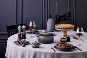 Een elegante tafelscène met een grijze zoutmolen op de voorgrond, omringd door stijlvol serviesgoed en een gedekte tafel, gezien vanuit een zijdelingse hoek.