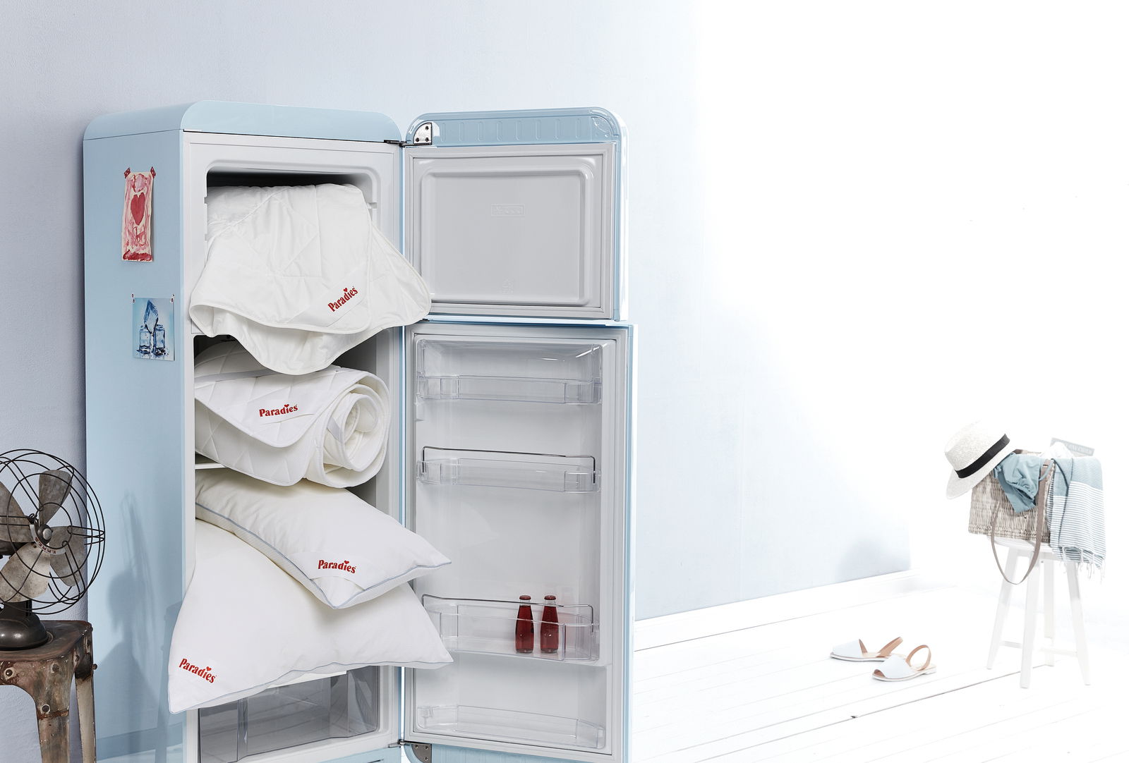 Paradies Kopfkissen SOFTY COOL BIO Ein geöffneter Kühlschrank mit mehreren Paradies Kopfkissen und Decken, die im oberen Fach gestapelt sind. Die Perspektive zeigt den Kühlschrank von vorne, mit einem hellen, minimalistischen Hintergrund.