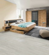 Moderne Schlafzimmermöbel mit einem dreitürigen Schwebetürenschrank, einem Bett mit integrierten Schubkästen und Nachttischen in Holzoptik. Perspektive: seitliche Ansicht des Schlafzimmers.