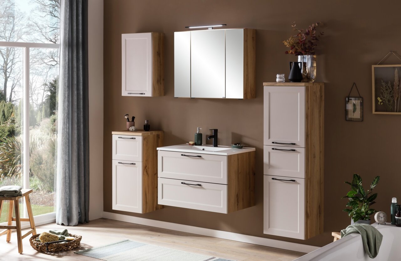 Modernes Waschtisch-Set in Holzoptik mit weißen Fronten, bestehend aus einem Waschbecken mit Unterschrank, einem Spiegelschrank und zusätzlichen Hängeschränken, aus der Perspektive eines hellen Badezimmers mit Blick auf den Garten.