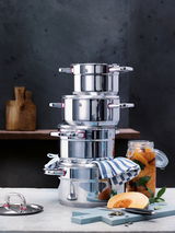Stapel von glänzenden Edelstahl-Töpfen aus dem Topfset Premium One 5-tlg., seitliche Perspektive, mit einem gestreiften Küchentuch und einem Glas mit eingelegtem Gemüse im Hintergrund.