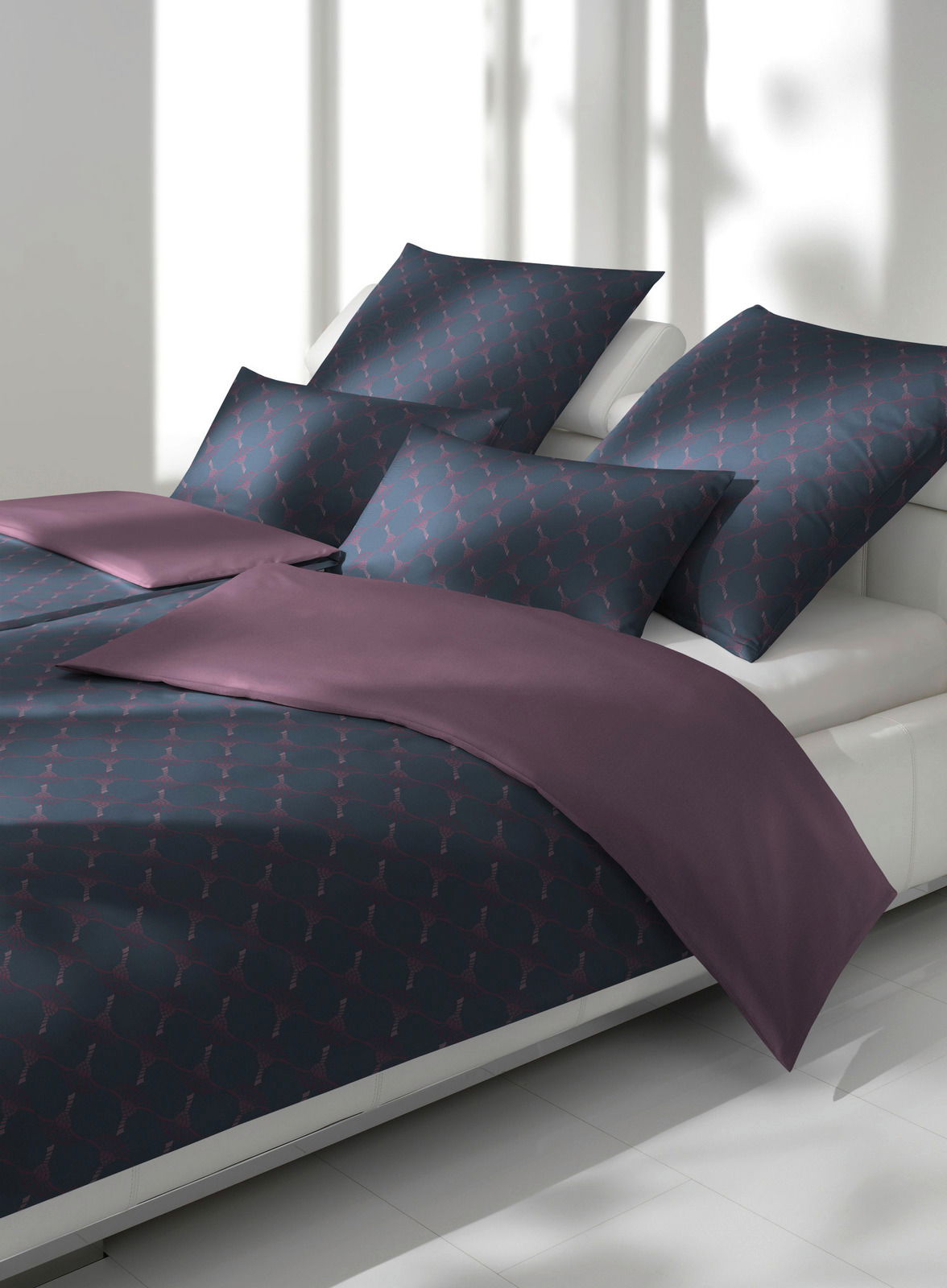 Bettwäsche-Set in dunklem Design mit geometrischem Muster und lila Akzenten, seitliche Perspektive auf einem weißen Bett.