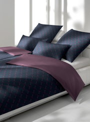 Bettwäsche-Set in dunklem Design mit geometrischem Muster und lila Akzenten, seitliche Perspektive auf einem weißen Bett.