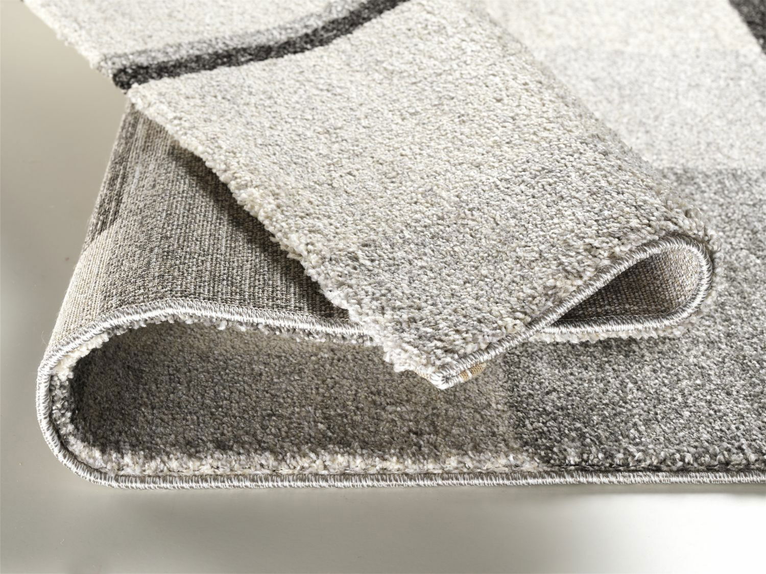 Nahaufnahme eines gefalteten Teppichs in Grautönen, der die Textur und Kanten zeigt.