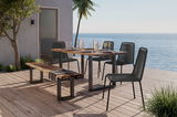 Moderner Stapelstuhl auf einer Terrasse mit Meerblick, neben einem Holztisch und einer Bank, aus seitlicher Perspektive.