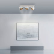 Deckenansicht eines modernen LED-Spots mit drei verstellbaren Leuchten, die ein Kunstwerk an der Wand beleuchten.