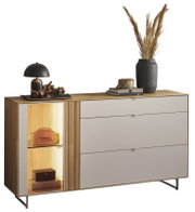 Modernes Sideboard aus Holz mit hellen Schubladenfronten und links beleuchteter Vitrine, dekoriert mit Lampe, Büchern und Vase mit Trockenblumen, frontale Perspektive