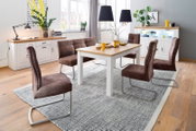 Moderne eetkamerset met een witte eettafel met houten blad, een bruine gestoffeerde bank en vier zweefstoelen op een grijs tapijt, gefotografeerd vanuit een licht schuin vooraanzicht op ooghoogte.