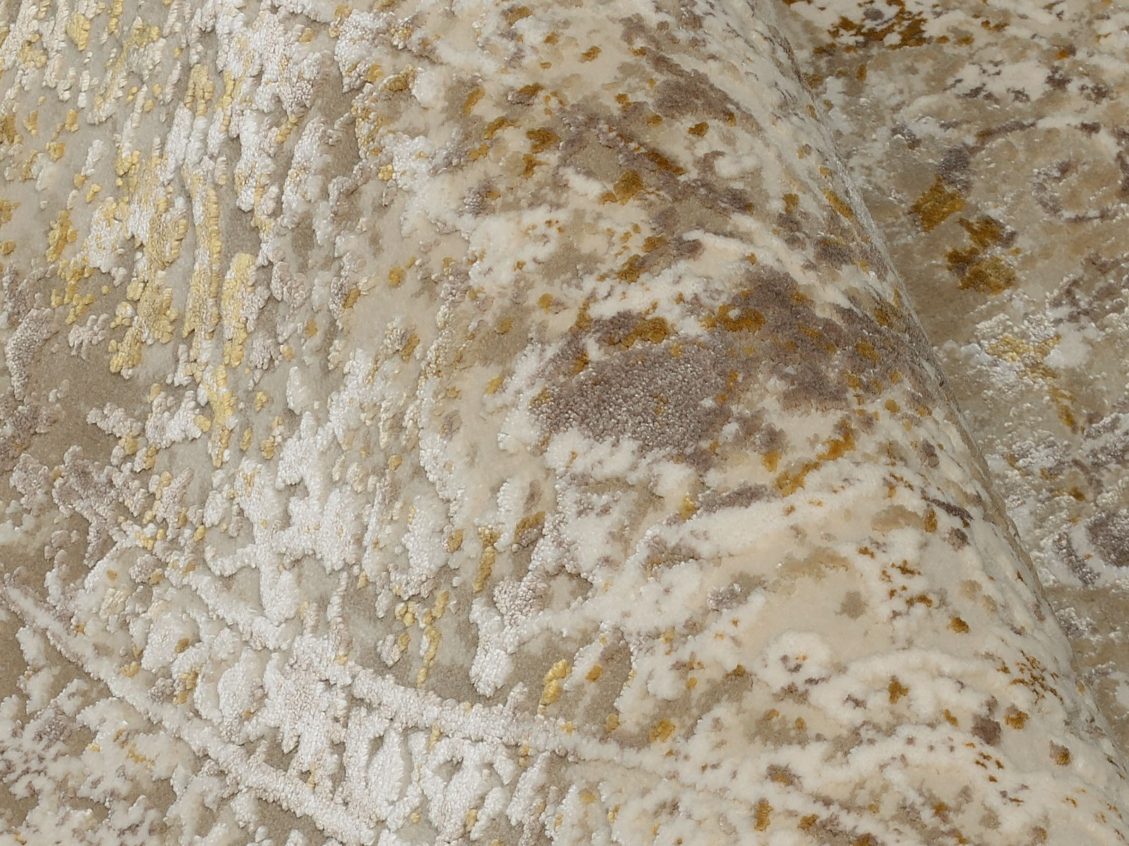 Nahaufnahme eines Designer Teppichs mit abstraktem Muster in Beige-, Grau- und Goldtönen, leicht gewölbt dargestellt.
