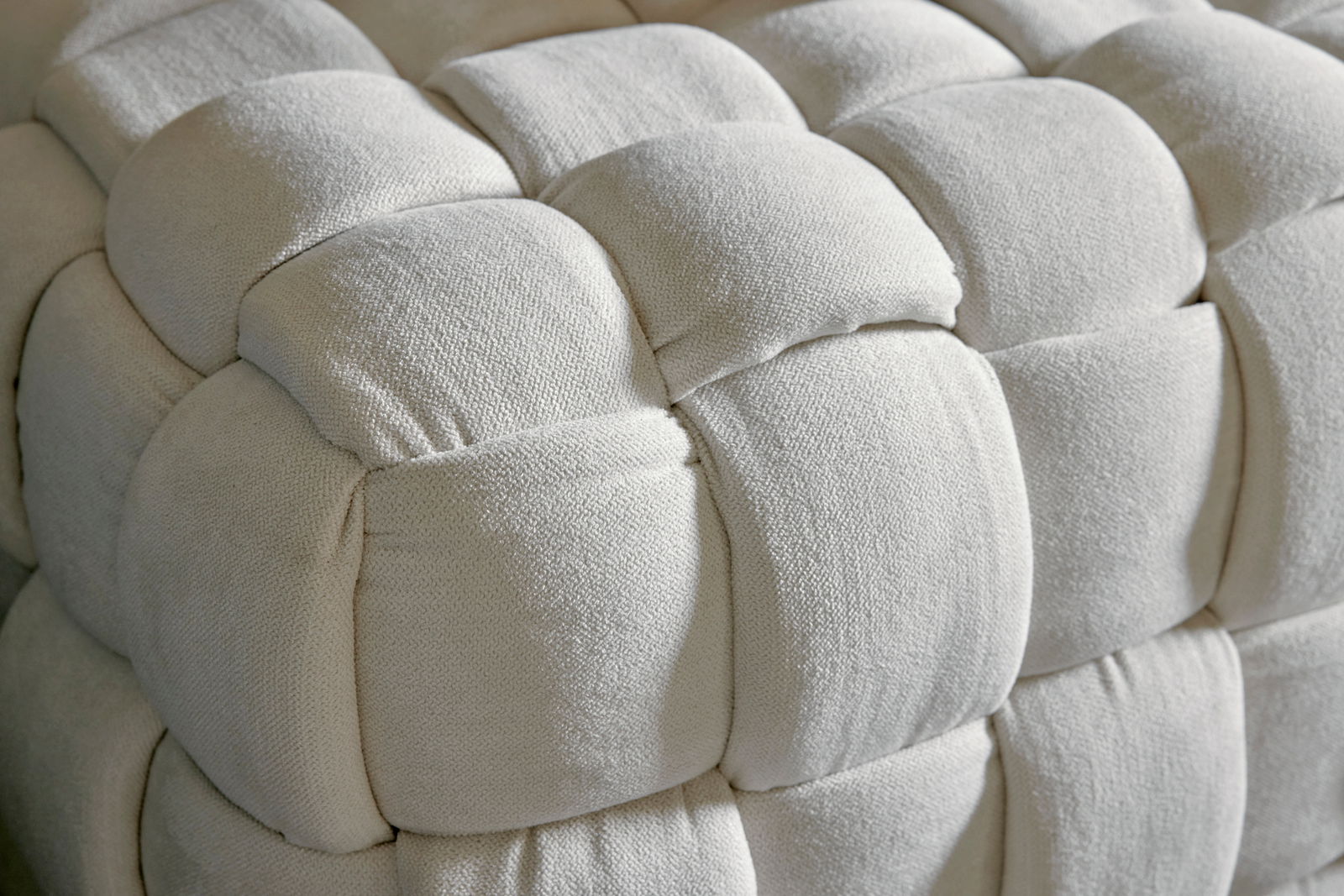 Nahaufnahme eines gepolsterten, cremefarbenen Hockers mit geflochtenem Design.