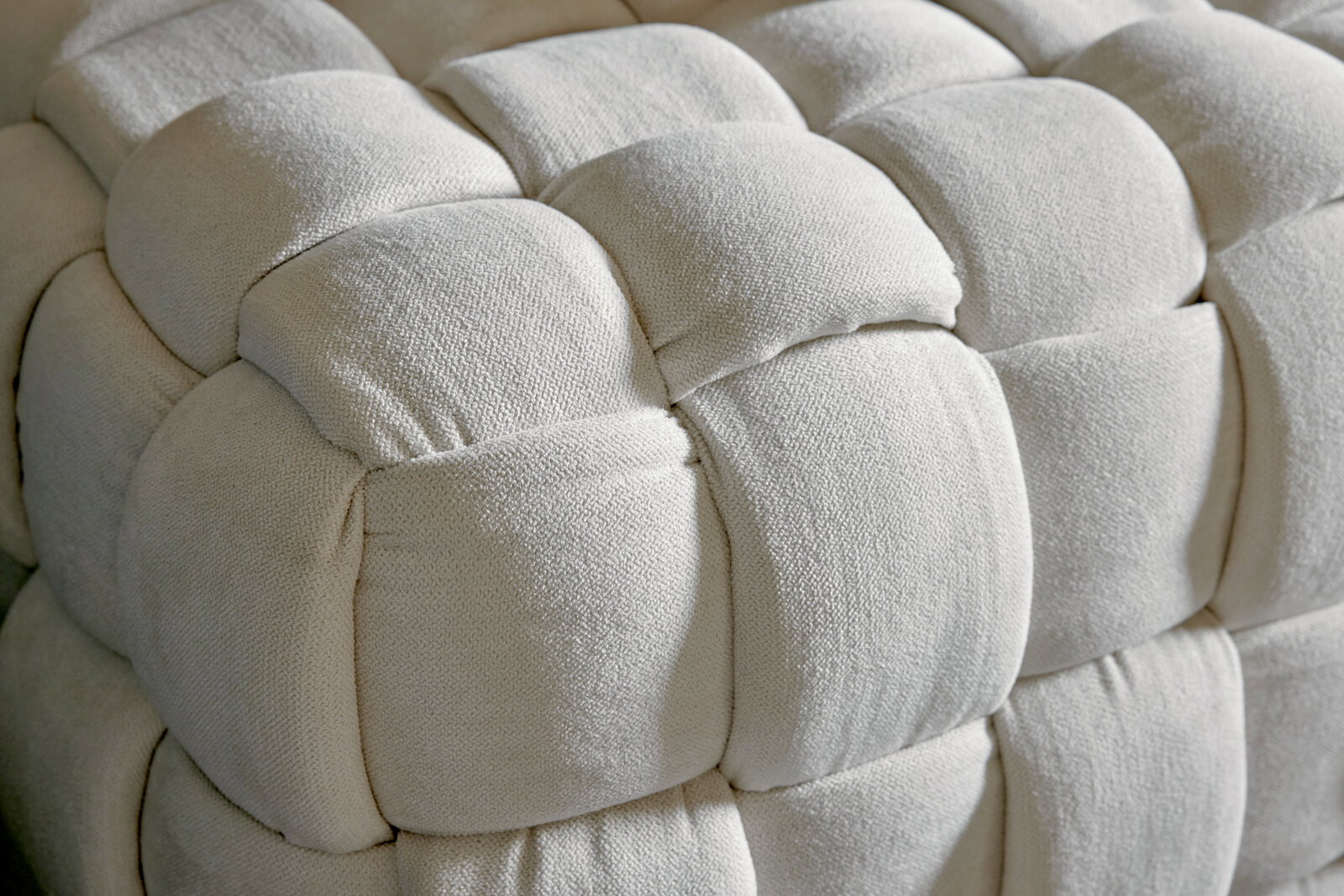 Nahaufnahme eines gepolsterten, cremefarbenen Hockers mit geflochtenem Design.