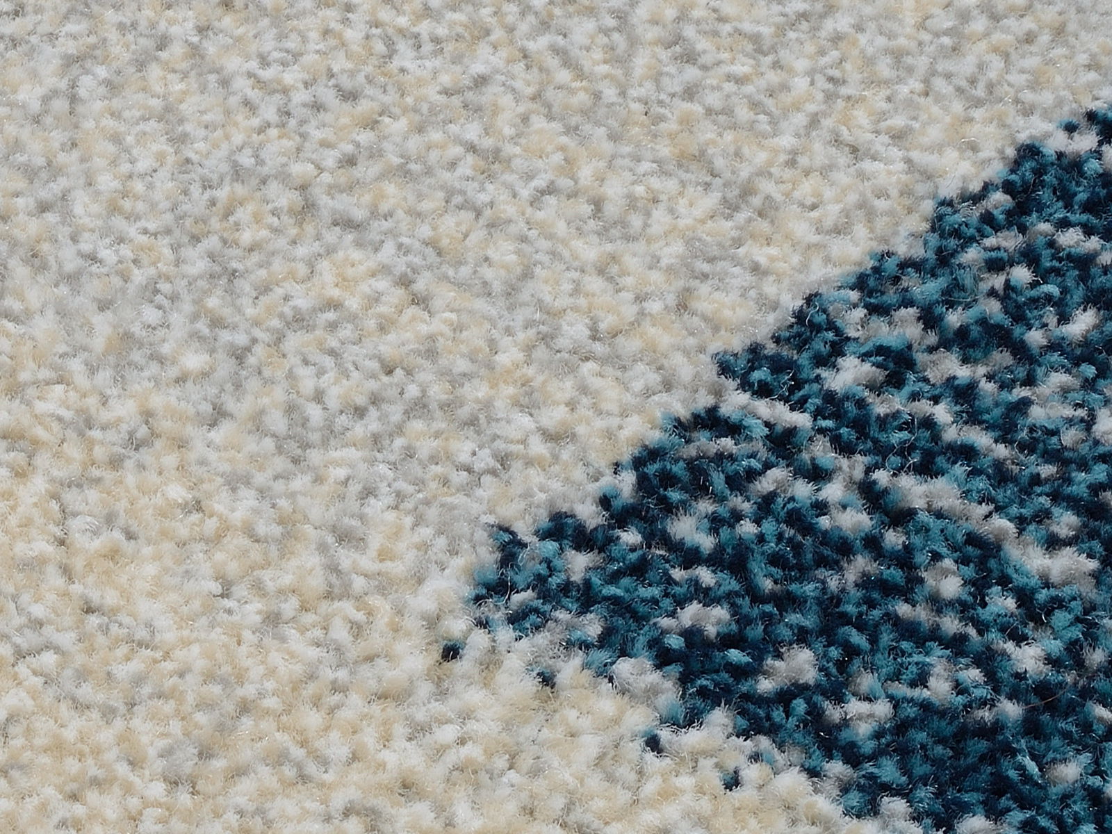 Nahaufnahme eines weichen Teppichs mit cremefarbenem und blauem Muster, perspektivisch von oben betrachtet.