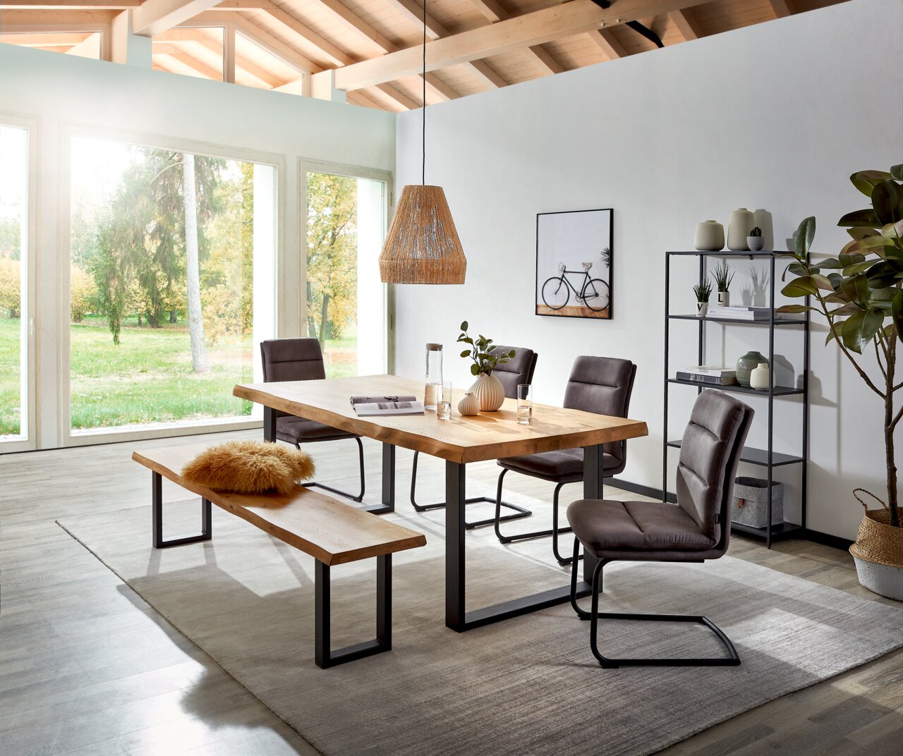 Landscape Bar COUNTRY II Moderne eetkamerset met een massief houten eettafel en een bijpassende houten bank op een zwart metalen onderstel, aangevuld met vier grijze zweefstoelen, gefotografeerd vanuit een licht schuin perspectief van voren in een lichte ruimte met grote ramen