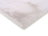 Nahaufnahme eines weichen, flauschigen Fellteppichs in hellem Grau, perspektivisch von der Seite aufgenommen.